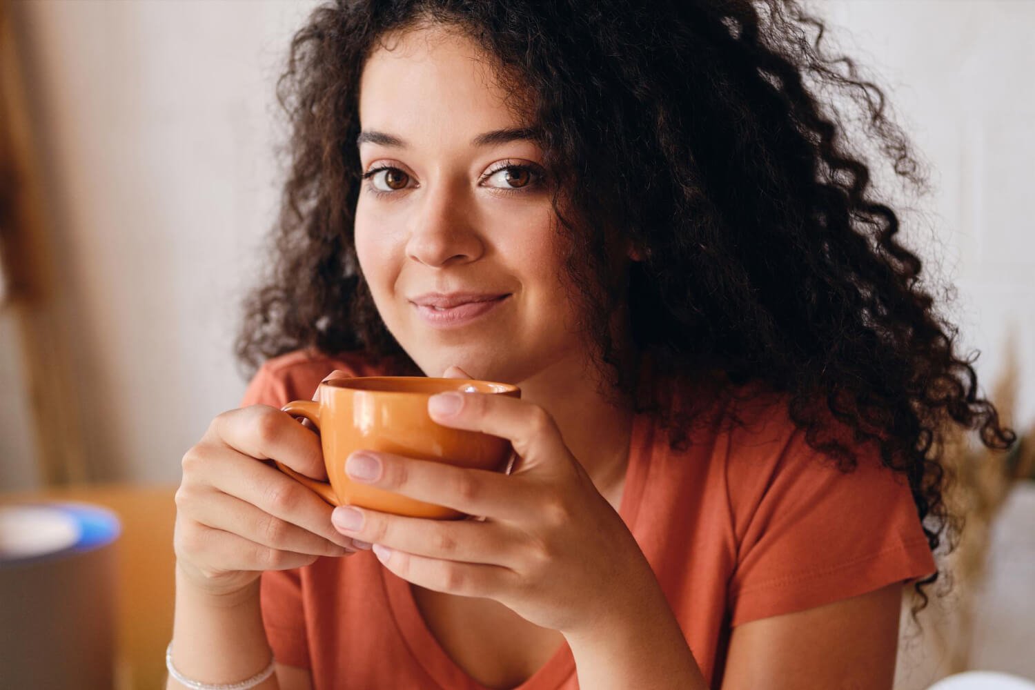 Mulher de cabelos cacheados segurando uma xícara de café. Dicas de alinhadores invisíveis na Clínica Croi Odontologia em Brasília.