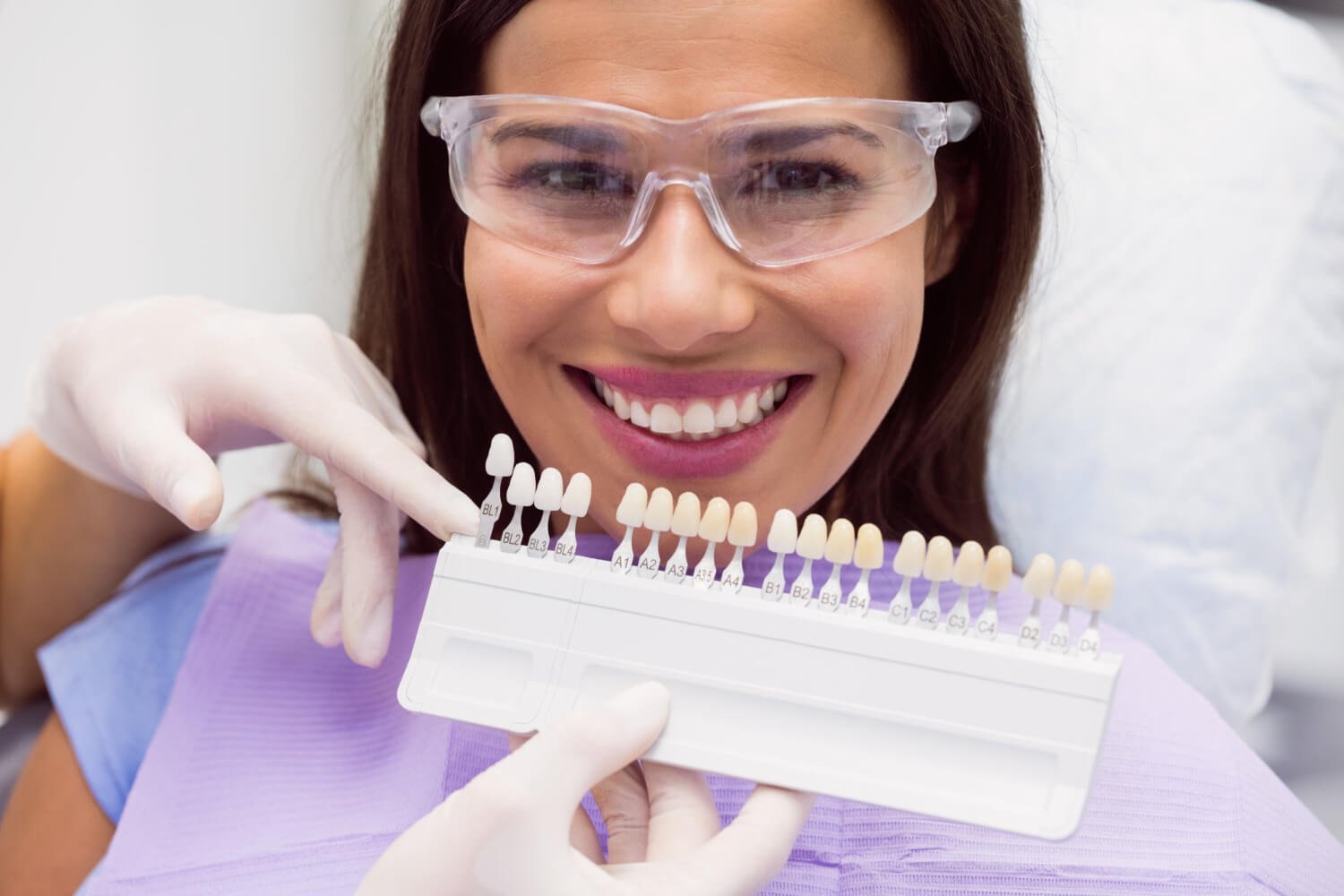Paciente sorrindo com escala de cores de dentes. Conheça as lentes de contato dental slim em Juiz de Fora na Cavasi Odontologia.