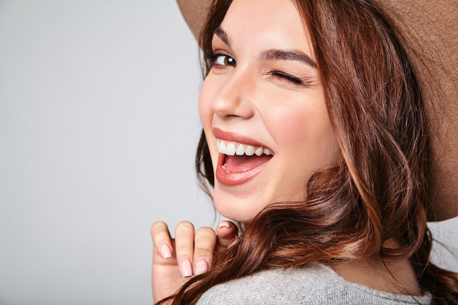 Mulher sorrindo e piscando com dentes perfeitos. Cuidados com lentes de contato dental na Clínica Croi Odontologia, Asa Norte, Brasília